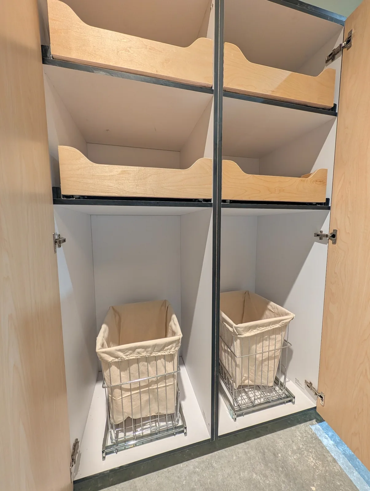Open cabinet with wood pull-out trays above two fabric-lined wire pull-out baskets.
